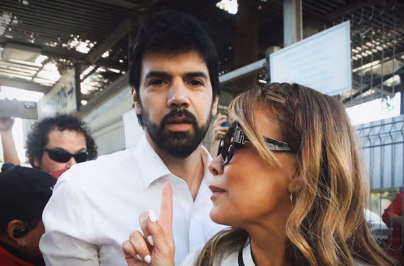 El diputado Joaquín Lavín León con un micrófono en una rueda de prensa, con un rostro serio o reflexivo.