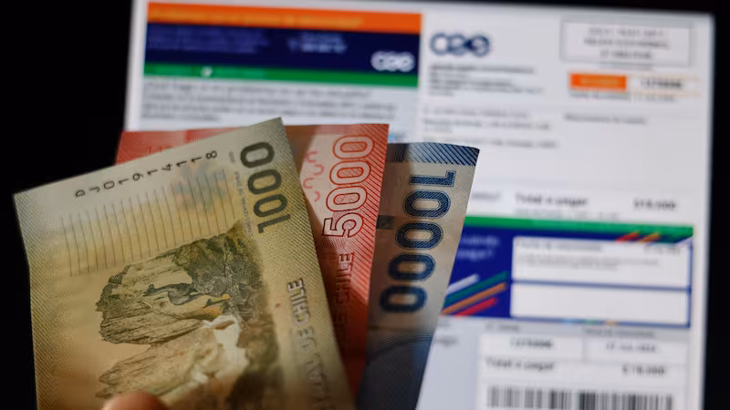 Una ampolleta encendida junto a una boleta de electricidad, simbolizando el alza en las cuentas de la luz en Chile.